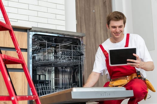 Portrait Of Male Technician Repairing Dishwasher In Kitchen using digital tablet