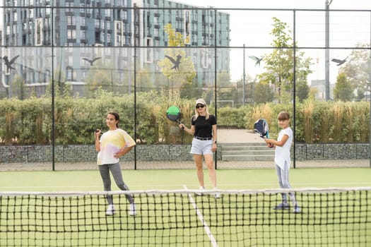 Young tennis trainer in activewear holding racket held by one of two cute girls while consulting her during individual training on stadium. High quality photo