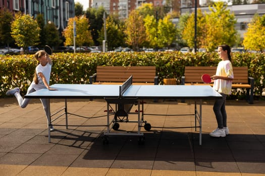 Young teenager girl playing ping pong. She holds a ball and a racket in her hands. Playing table tennis outdoors in the yard. High quality photo