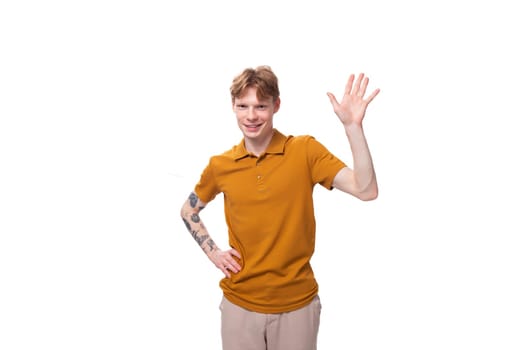 young charming red-haired man dressed in a mustard t-shirt points his hand to the side.