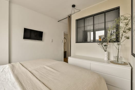 a bedroom with a bed, dresser and tv mounted on the wall in front of the bed is also white