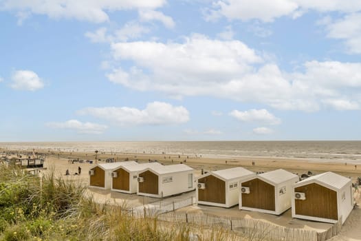 some beach huts on the sand dunes in front of an ocean and blue sky with white puffy clouds above