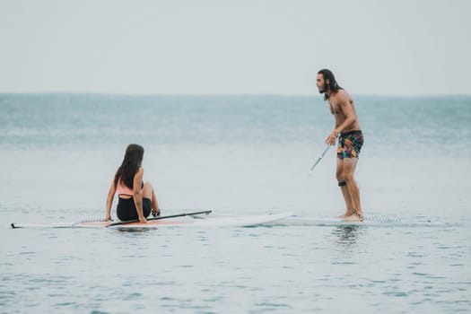 Sea woman and man on sup. Silhouette of happy young woman and man, surfing on SUP board, confident paddling through water surface. Idyllic sunset. Active lifestyle at sea or river