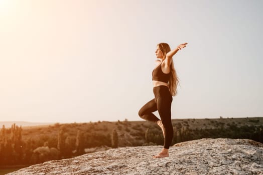 Well looking middle aged woman with long hair, fitness instructor in leggings and tops doing stretching and pilates on the rock near forest. Female fitness yoga routine concept. Healthy lifestyle.