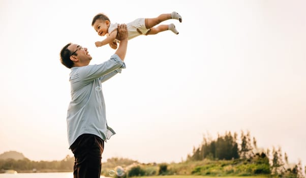 Playful family moment, father holds happy little boy up high, throwing up in sky on his birthday. cheerful child enjoys moment of freedom and joy, while the loving dad captures precious memory forever