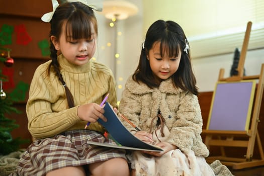 Image of happy little siblings reading a storybook together in cozy living room decorated for Christmas.