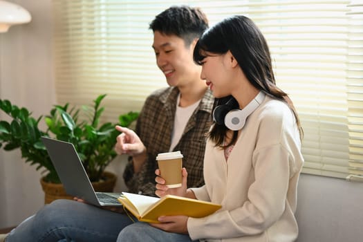 Asian college students using laptop discussing research and learning tasks together.