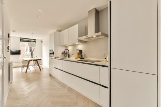 a kitchen with white cabinets and wood flooring in the middle of the room, looking towards the dining area