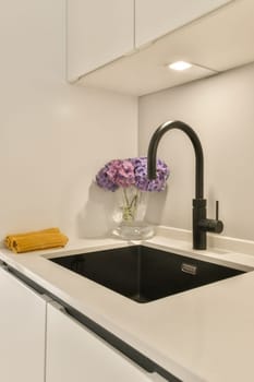 a kitchen sink with flowers in a glass vase on the countertop and black fauced fae over it
