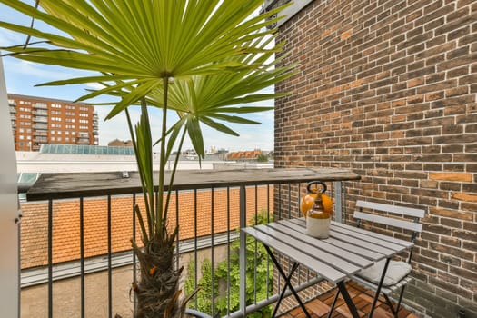 a balcony with a palm tree in the center and an empty table on the other side, next to a brick wall