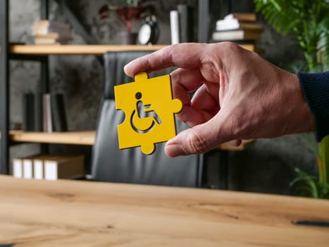 A hand holds a puzzle disabled person symbol in the workplace as a symbol of accessibility and inclusion.