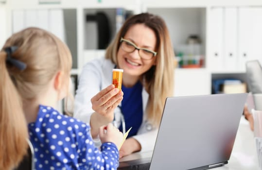 Beautiful smiling female doctor hold in arms pill bottle and offer it to child visitor closeup. Panacea or life save antidepressant from legal store prescribe vitamin medic aid for healthy lifestyle