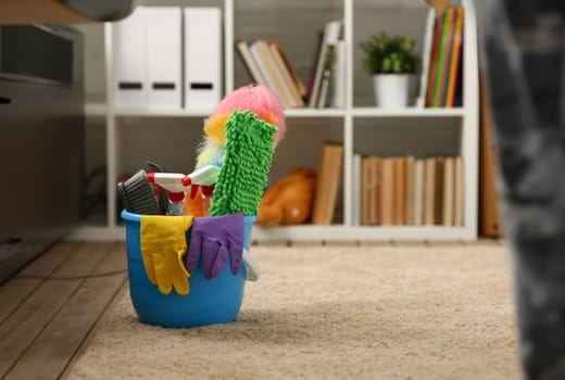 A bucket with cleaning equipment stands on the carpet in the room