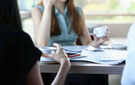 business people in cafe coffee break at table hold cup of coffee in arms closeup