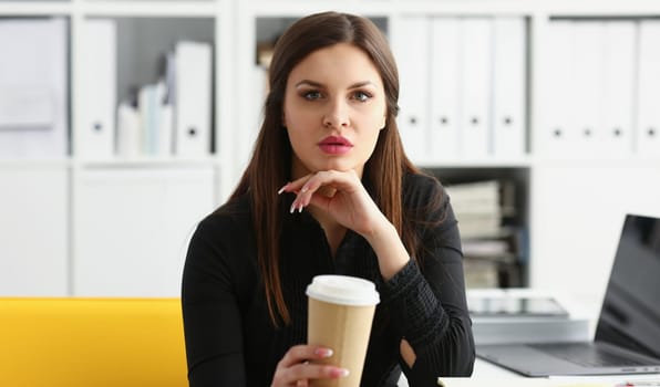 Businesswoman at workplace in office portrait during break drinks coffee from white cup smiling. Looking at camera creates visibility of work and success causes trust.