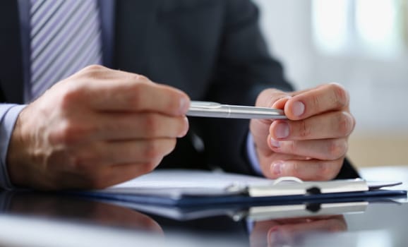 Male arm in suit and tie fill form clipped to pad with silver pen closeup. Sign gesture read pact sale agent bank job make note loan credit mortgage investment finance chief legal law concept