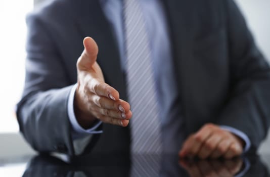 Man in suit and tie give hand as hello in office closeup. Friend welcome mediation offer positive introduction thanks gesture summit participate approval motivation male arm strike bargain