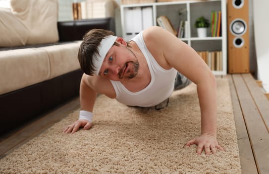 A young handsome man with excess weight makes the first fitness training at home on carpet. Is wrung out and he ery heavily loaded does not stimulate to lose weight.