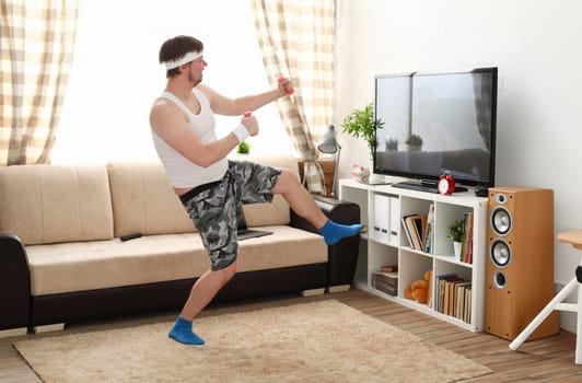 Young handsome man in shorts and vest holds pink dumbbells in hand. Watch tv lessons single combats is practicing receptions of sensei one home fitness indoor training independent education remotely