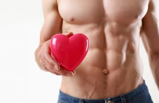 Athletic man holds a heart in his hand abs traning