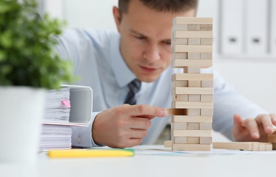 Businessman plays in strategy hand rearranging wooden blocks involved during break at work in office sitting table gaming pile fun joy pastime concept