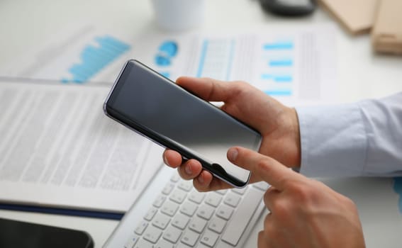 A businessman holds a new smartphone in his hand The mobile application market shows a display. You can insert your image for advertising or financial statistics.