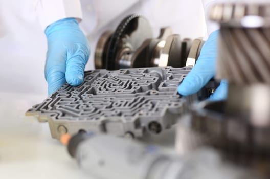The auto repair service repairman automatic gearboxes holds in his hand in blue protective gloves. Hydroblock detail dehydrates the diagnostics and estimates the detail test transmission closeup.