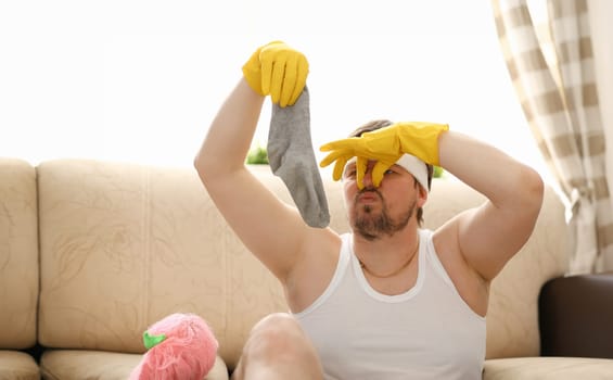 Young masculinity bachelor wife left alone at home and before her arrival collects scattered socks. Around the apartment for washing closes her nose with her fingers unpleasant smell.