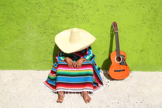 lazy typical mexican man with sombrero sitting on green wall having a nap