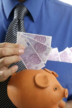 businessman insert euro notes in clay piggy bank