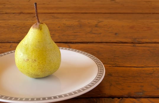 one pear on white plate posed on old wood table