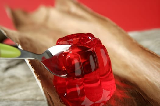 Jelly in red strawberry color in green spoon over wood