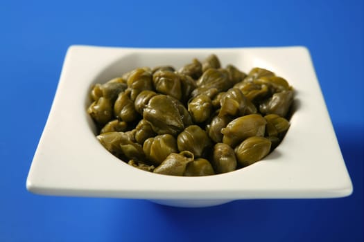 Capers with vinegar snack on a white plate, blue background