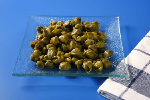 Capers with vinegar snack on a transparent plate, blue background