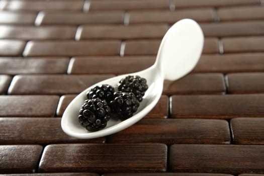 Black berries in a white spoon, wooden background