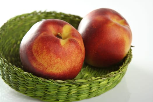 Summer fruits, two red peaches in a green basket