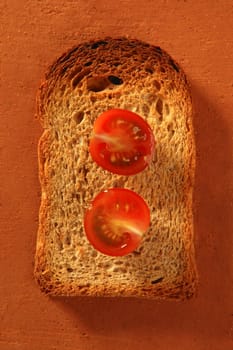 Toasted bread slices and cherry tomatoes on orange clay background