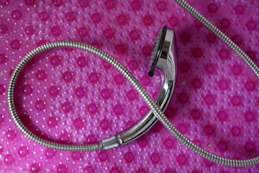 Bathroom chrome shower head with silver hose over pink background
