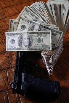 Dollar notes and gun, black pistol over crocodrile black fake leather