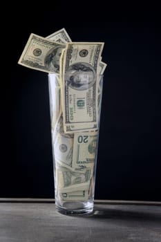 High glass full of dollar notes over black background
