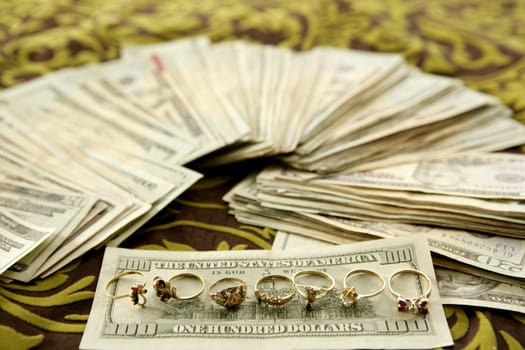 Dollar notes and gold rings over tablecloth, studio recreation