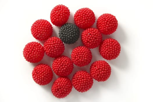 one black candy berry isolated between red candy jelly berries