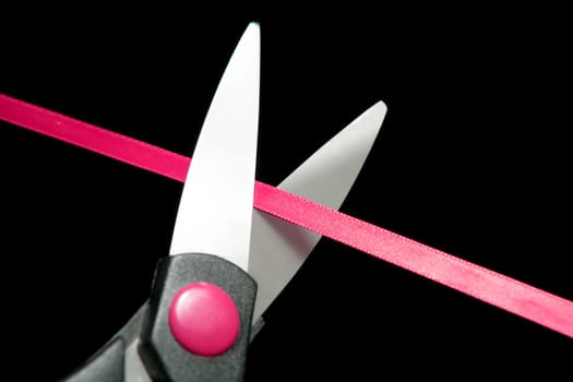 Red tape going to be cutted by scissors. Black background
