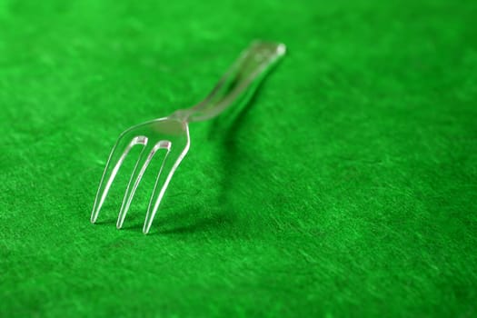 Transparent plastic fork on a textured vivid green background