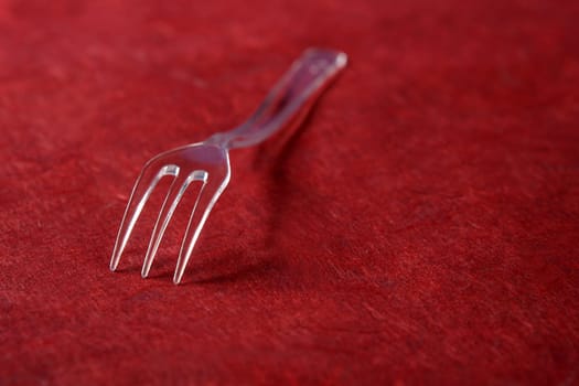Transparent plastic fork on a textured vivid red background