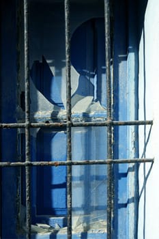 Jail fence over blue mediterranean blue window, broken glass
