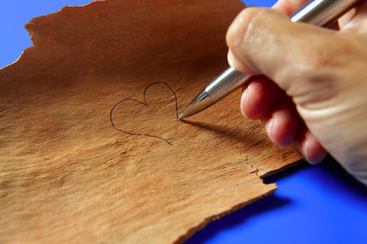 Human hand writing, drawing with a pen a heart on wood, valentines day