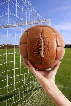 Football vintage ball in hand net soccer goal green grass background
