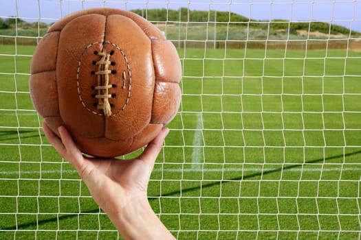 Football vintage ball in hand net soccer goal green grass background