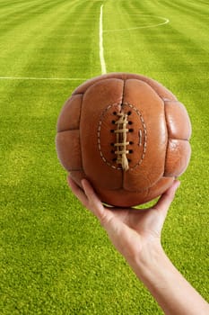 Aged vintage retro football leather ball in man hand grass field